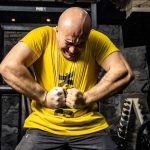 Bald muscular man in yellow t-shirt showcasing strength in a gym, highlighting intense dedication.